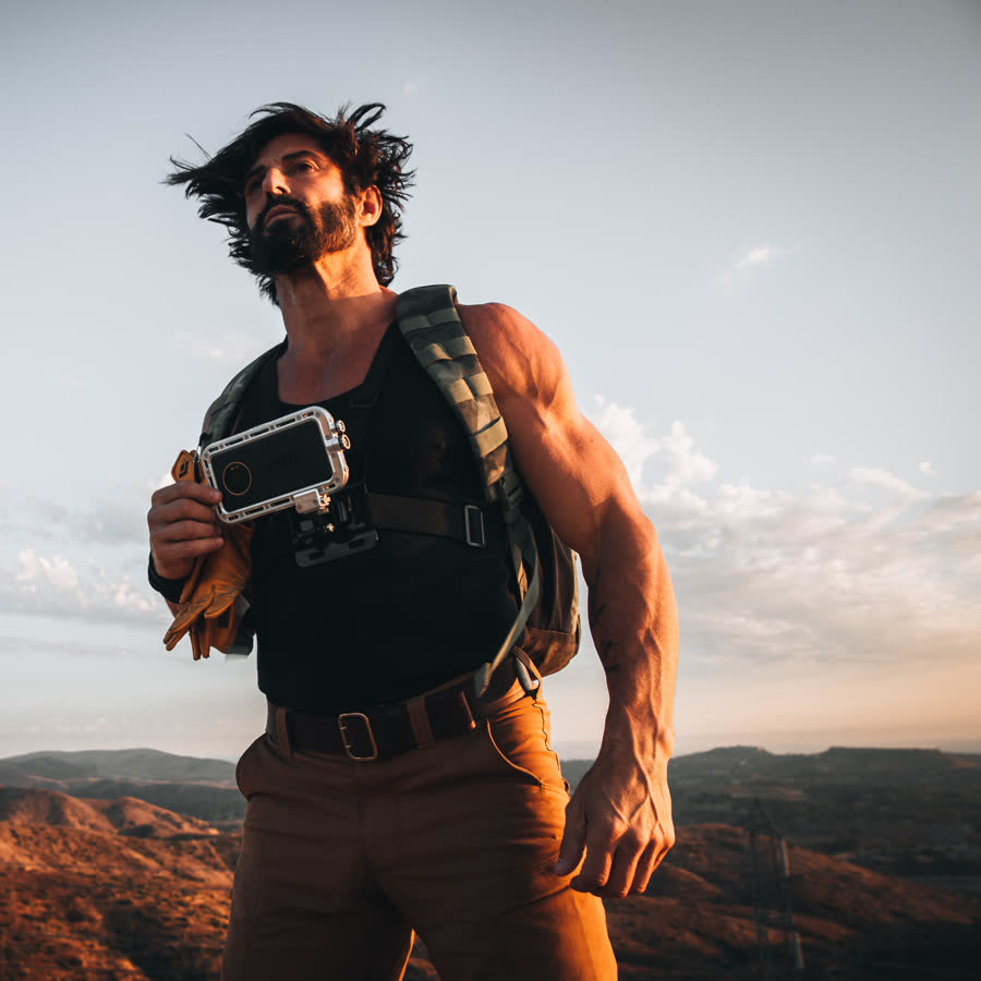 Man on a ridge at dusk holding a phone in an Atmos rugged waterproof case